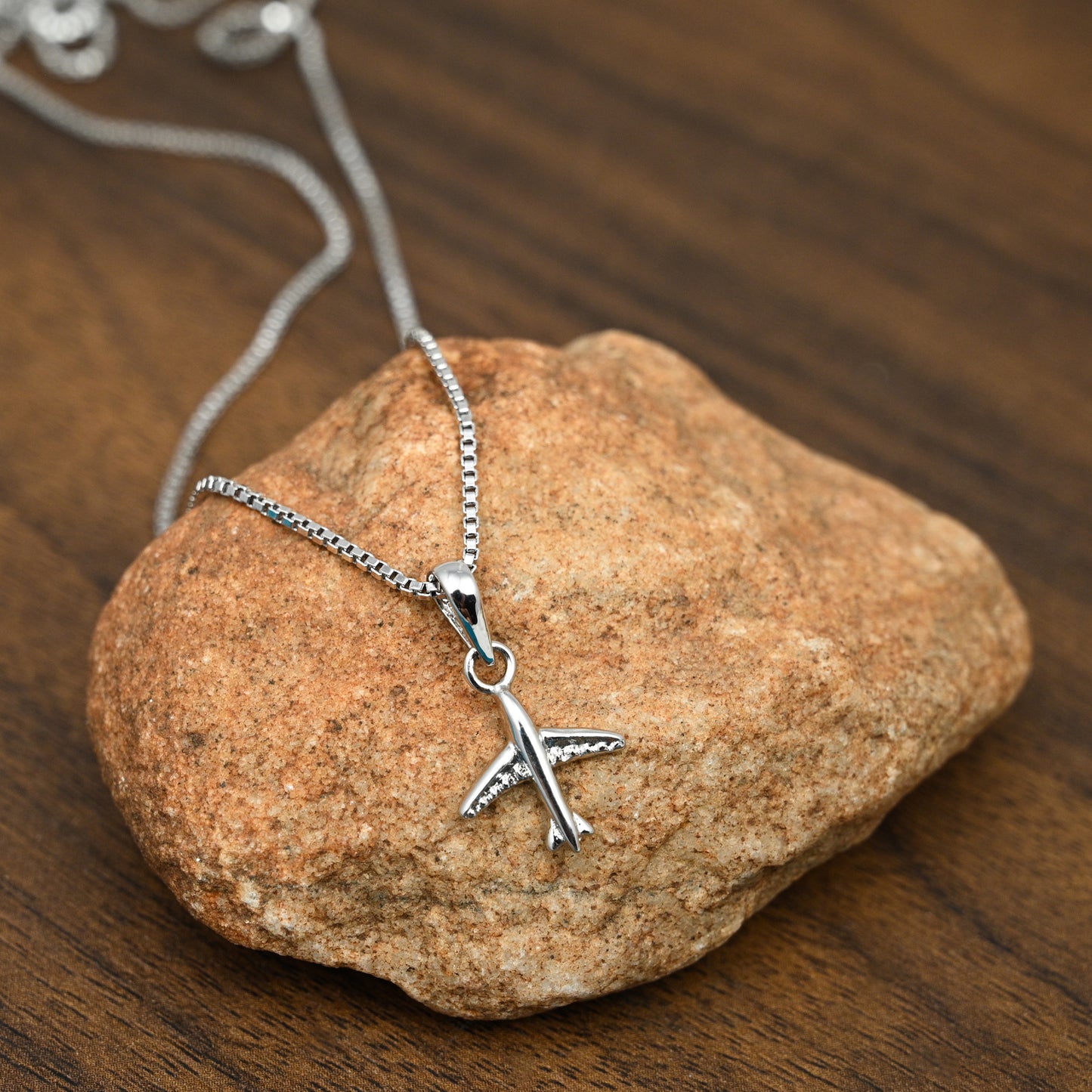 Aeroplane shaped sterling silver pendant with chain in white rhodium beautifully displayed on a rock.
